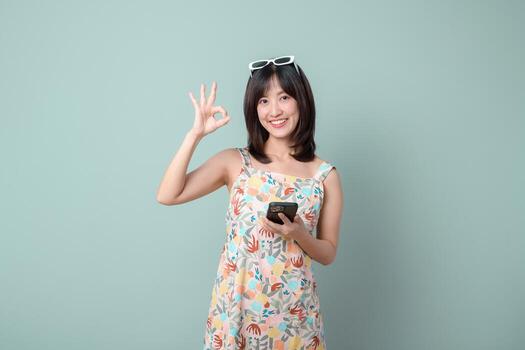 Sureste asiático mujer sonriente y participación móvil teléfono utilizando Internet solicitud demostración bueno gesto con mano en vistoso vestir foto