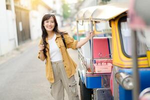 Southeast asian woman travel concept with happy smile stands beside colorful tuk tuk on sunny street ready for adventure and exploration in urban setting photo