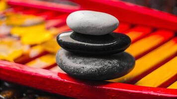 A zen stack of three smooth stones balanced on a red and yellow painted surface close up photo