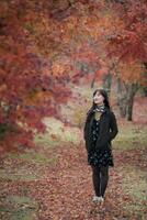 Southeast asian woman enjoys peaceful walk in autumn forest surrounded by colorful red and orange leaves creating warm and serene atmosphere in nature photo