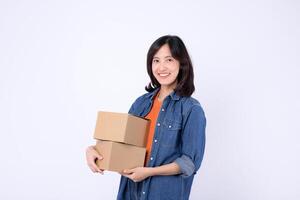 Southeast asian woman is happily shopping online and holding two cardboard boxes while wearing denim jacket and orange shirt against white background photo