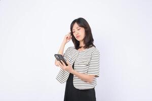 Southeast asian woman is using mobile phone to browse internet with thoughtful expression while standing against plain white background in casual clothing photo