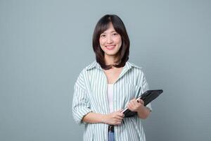 Southeast asian woman smiling confidently while holding tablet, representing online shopping and digital lifestyle with casual striped shirt and relaxed pose photo