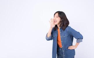 Southeast asian woman wearing denim is enthusiastically advertising with joyful expression and hand near her mouth on white background photo