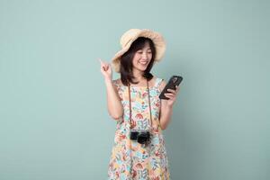 Southeast asian woman happily uses mobile phone to explore internet application while wearing floral dress and straw hat with camera hanging around her neck photo
