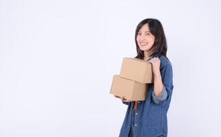 Southeast Asian woman smiling while shopping online holds two cardboard boxes in casual denim outfit against white background showing happiness and convenience photo
