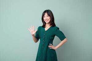 Southeast asian woman in green dress smiling and advertising with friendly hand gesture against plain background photo