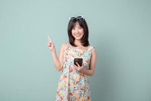 Southeast asian woman smiling happily while holding mobile phone and pointing up as if explaining internet application on pastel background photo