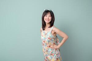 Happy Asian woman in floral dress smiling confidently with sunglasses on head, standing against pastel green background photo