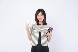 Asian woman holding cash and smartphone, smiling against white background, concept of mobile banking and financial success photo