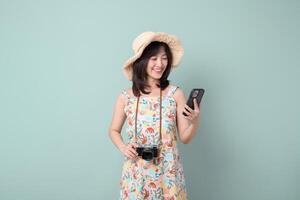 Southeast asian woman in summer dress and straw hat holding camera and smartphone smiling while planning travel against pastel background photo