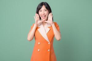 Southeast asian woman in orange suit smiling and calling out with hands near mouth on green background cheerful expression photo