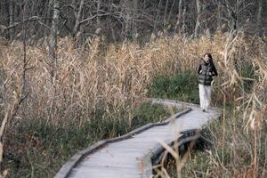 Southeast asian woman enjoys travel concept walking on wooden path through dry grass and bare trees in peaceful natural setting with calm and reflective mood photo