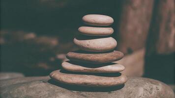 A stack of smooth stones balanced on a larger rock in a dimly lit outdoor setting photo