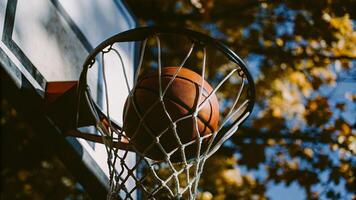 A basketball going through a net with a backdrop of trees and a blue sky outside photo