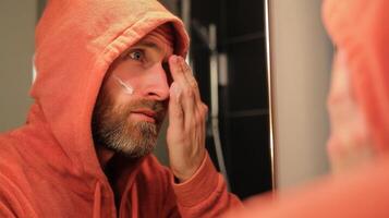 A man in an orange hoodie looking in the mirror photo