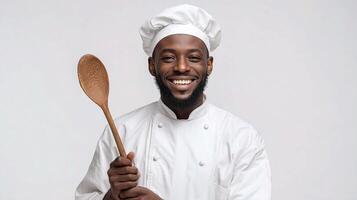 A smiling black man in a chef hat holding a wooden spoon photo