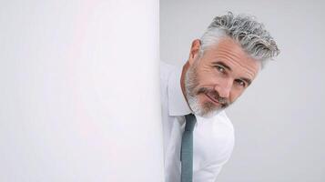 A man with a white beard and tie peeking out from behind a white wall photo