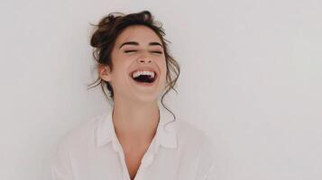 A woman laughing while standing in front of a white wall photo