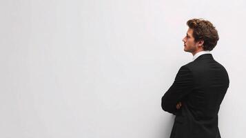 A man in a suit standing against a white wall photo