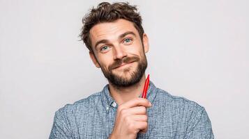 A man with a beard and a blue shirt is holding a red pencil photo
