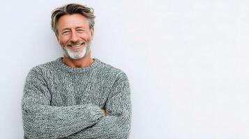 A man with a gray beard and sweater standing in front of a white wall photo
