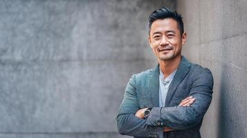 Asian man with arms crossed leaning against a wall photo