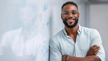 A smiling black man in glasses standing in front of a whiteboard photo