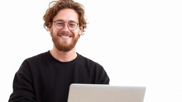 A man with glasses and a beard is smiling while using a laptop photo