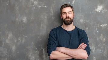 A man with a beard and a blue shirt is standing in front of a wall photo