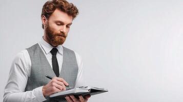 A bearded man in a vest and tie writing on a notepad photo