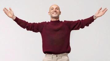 A bald man in a maroon sweater is standing with his arms outstretched photo