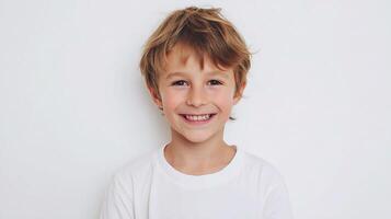 A young boy is smiling in front of a white wall photo