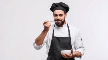 A male chef holding a spoon and eating a bowl of soup photo
