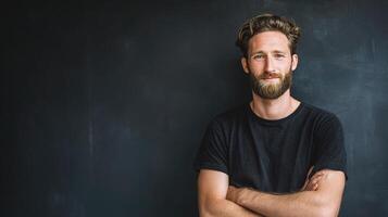 A man with a beard and a black shirt standing in front of a blackboard photo
