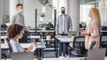 Meeting and new tasks from manager during covid-19 epidemic. Woman in business suit and protective mask speaks with workers, african american lady takes notes in office interior, panorama, empty space photo