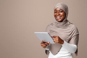 Smiling Black Lady In Hijab Using Digital Tablet, Shopping Online Or Browsing Social Networks, Muslim Woman In Headscarf Enjoying Modern Technologies, Standing Over Light Studio Background, Copy Space photo