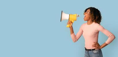 Amazing Offer. Young Black Woman Shouting With Megaphone, Making Announcement, African American Lady With Loudspeaker In Hands Sharing News, Standing Over Blue Background, Panorama, Copy space photo