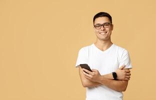 Social media, app, modern communication and lockdown. Attractive cute zoomer student in glasses, white t-shirt with smart watch hold smartphone and texting message, isolated on light sand background photo
