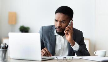 Concerned businessman talking on cell phone and looking at laptop screen, trying to reach technical support to solve issue with his computer, panorama photo
