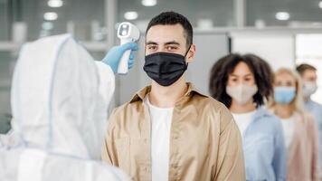 Checking temperature morning before work. Man in hazmat suit control first symptoms of illness at workers in protective masks in office, during covid-19 epidemic, empty space, close up photo