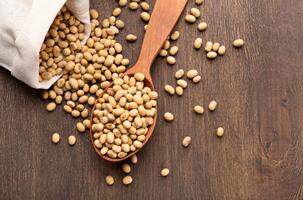 Soybeans scattered on rustic table with wooden spoon from paper bag, top view, free space photo