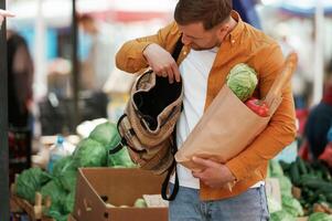 Opening, the backpack. With products in paper bag. Handsome man is on the street market or bazaar photo