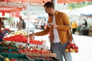 With, a shopping list. Vegetables and fruits. Handsome man is on the street market or bazaar photo
