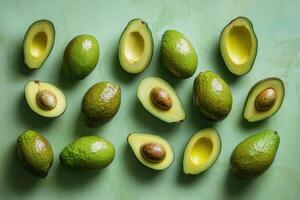 Fresh avocados arranged on a green surface with some cut open photo