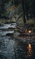 Cozy riverside retreat featuring a vintage chair and glowing lantern in a serene forest setting photo