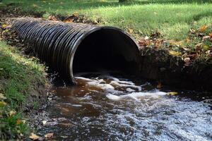 Drainage pipe emptying polluted water into small creek in autumn photo