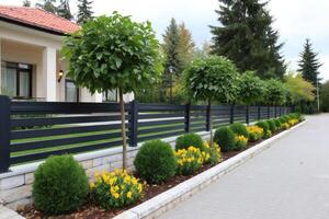 Modern horizontal slat fence with flowerbed and trees bordering a paved path photo