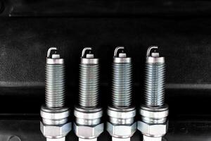 Car Spark Plugs, Close-up of four new iridium spark plugs are lined up against a dark background. DIY engine repair photo