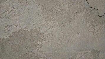 A close-up of a rough, worn-out concrete wall with a gritty texture, featuring cracks and crevices. The color is a dull, gray with subtle variations in shade, showing off the uneven surface. photo